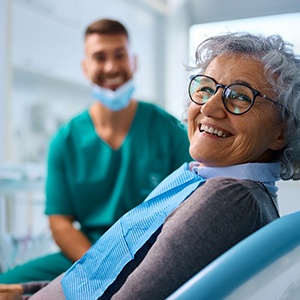 Woman with black glasses smiling while sitting in treatment chair