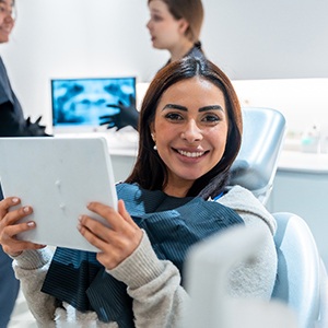 Patient smiling while holding mirror in treatment chair