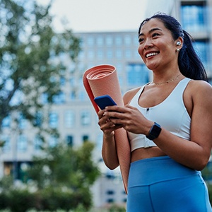 Smiling woman with yoga mat walking in park